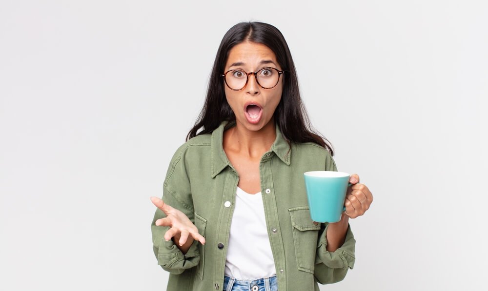 Mulher segurando uma xícara com café e com cara de assustada