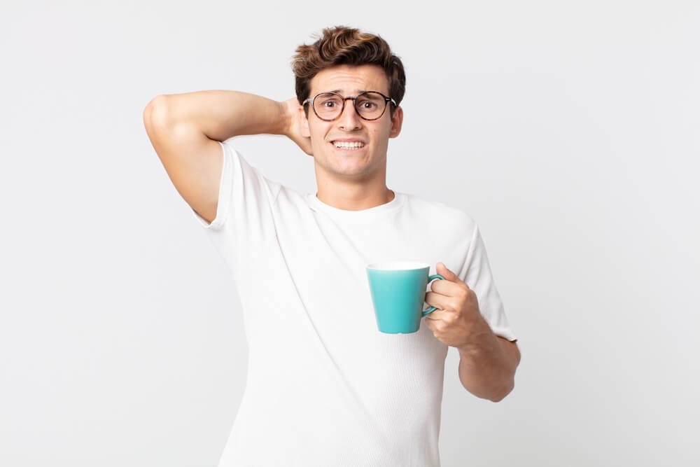 Rapaz com um copo de café na mão e cara de quem tomo muito café